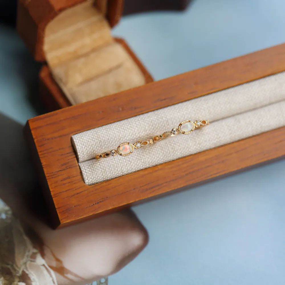 Two gold opal rings displayed side-by-side inside a slotted wooden jewelry presentation box.