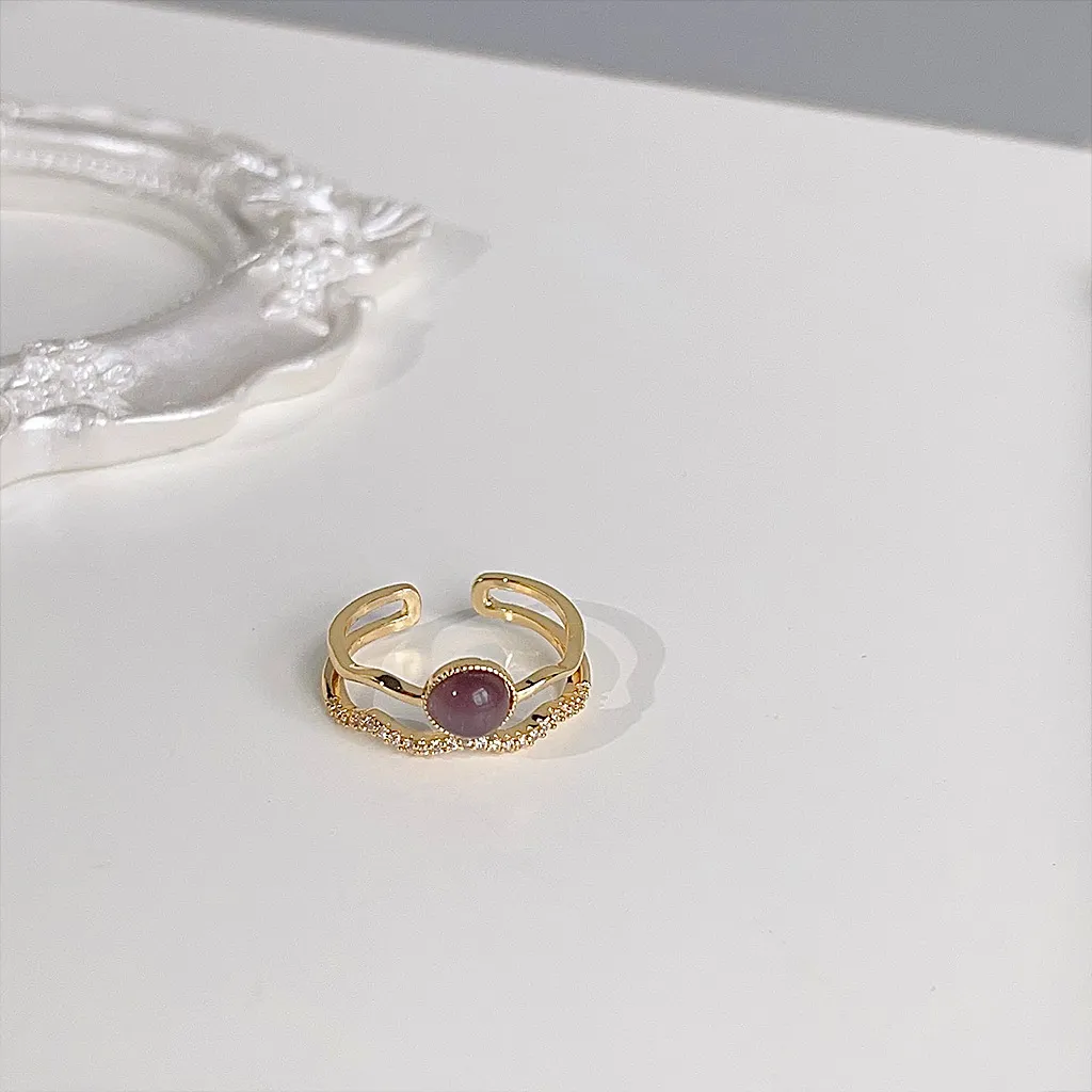 Gold-plated adjustable double-band ring with a purple cat's eye stone on a white surface.