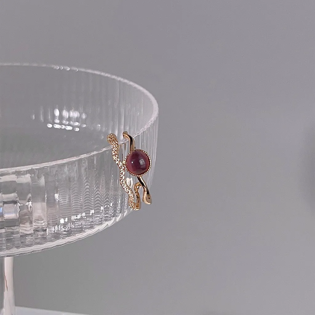 Cat's eye double-band ring balanced on the edge of a clear glass stand.