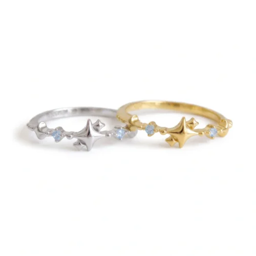 Silver and gold celestial starburst rings with small blue stones resting on a white background.